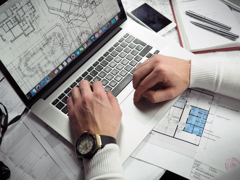 Laptop showing floor plans next to printed drawings